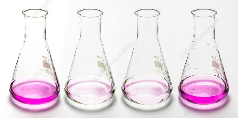 Cận cảnh một bình tam giác chứa dung dịch không màu đang được nhỏ từ buret, tại điểm tiếp xúc dung dịch chuyển sang màu hồng, cho thấy điểm cuối của chuẩn độ.